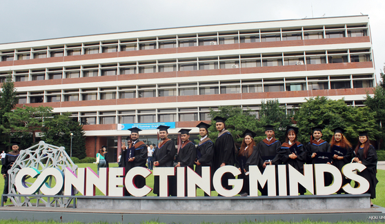 International students at Ajou University Graduate School of International Studies celebrate their graduation in July 2022 behind a structure that represents Ajou’s educational philosophy, “A connected world, collaborative intelligence.” [YONHAP]