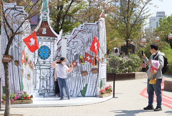 People pose in front of a cardboard box drawing depicting a scene in Switzerland at the Gyeongui Line Book Street in Mapo District, western Seoul, on Sunday. This year marks the 60th anniversary of diplomatic relations between Korea and Switzerland. [YONHAP]