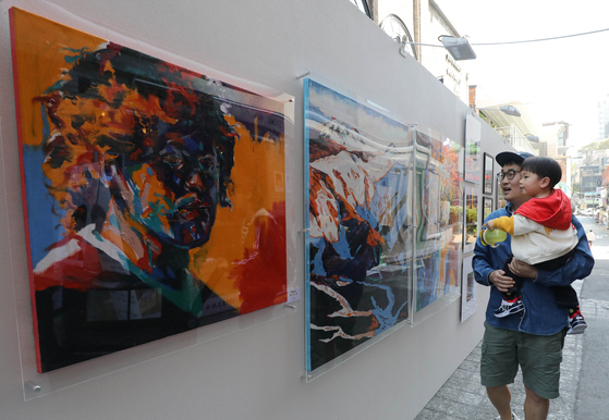 A father and child look at artwork displayed at the art exhibition held on Sunday in Itaewon, central Seoul. The exhibition has been held as a part of the ″Hey, Itaewon″ project to revive the neighborhood after last October's tragic crowd crush. [NEWS1]