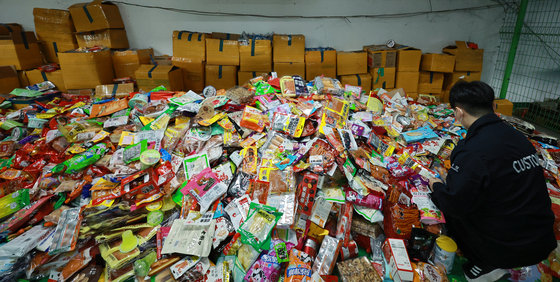 An official from Seoul Regional Customs in Gangnam District, southern Seoul, looks at a pile of seized processed foods on Tuesday. The customs office said it arrested a man in his 30s on charges of violating customs and import food safety management laws by importing around 23,000 processed food items valued at around 270 million won ($204,000). [YONHAP]