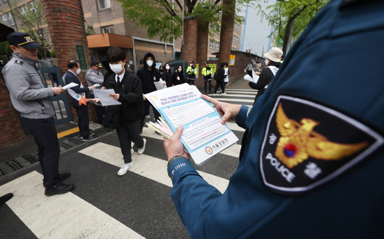 Police hand out notices to students alerting them of potential drug crimes in front of a high school in Songpa District, southern Seoul on Tuesday. [YONHAP]