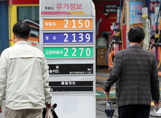 People walk past a sign board showing oil prices in Seoul on Tuesday. The Ministry of Economy and Finance announced Tuesday it would extend tax cuts on fuel for four months through August. [NEWS1]