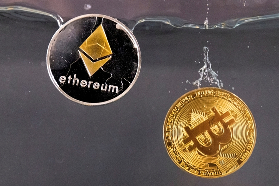 Souvenir tokens representing cryptocurrency Bitcoin and the Ethereum network, with its native token ether, plunge into water in this illustration taken on May 17, 2022. [REUTERS/ YONHAP]