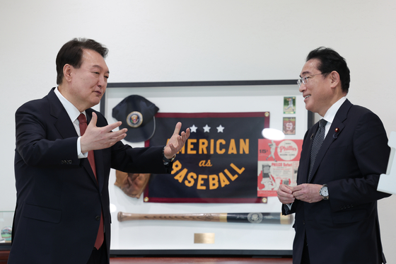 Korean President Yoon Suk Yeol, left, chats with Japanese Prime Minister Fumio Kishida, in front of U.S. President Joe Biden’s gift of baseball memorabilia from Yoon’s state visit to Washington at the Yongsan presidential office in central Seoul Sunday during their bilateral summit. [PRESIDENTIAL OFFICE]