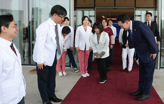 President Yoon Suk Yeol, right, sends off health care workers who fought on the front lines of the Covid-19 pandemic after a meeting of the Central Disaster and Safety Countermeasure Headquarters at the Yongsan presidential office in central Seoul on Thursday, where he declared a lowering of the national crisis level for Covid-19. [PRESIDENTIAL OFFICE]
