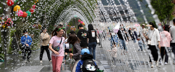Visitors to Gwanghwamun Square in central Seoul walk under sprinklers on Sunday. [NEWS1]