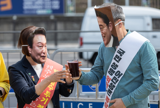 Members of the parliament protest the planned discharge of treated water from the ruined Fukushima nuclear power plant in front of the presidential office in Seoul on Monday. The parliamentarians are wearing masks with the faces of Korean President Yoon Suk Yeol, left, and Japanese Prime Minister Fumio Kishida, right, and handing over a glass of water meant to symbolize treated water. [NEWS1] 