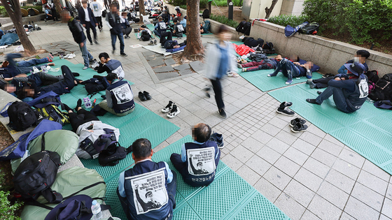 A person passing through Cheonggye Plaza and a group of labor union members resting there during their two-day really against the government on Wednesday. [YONHAP]