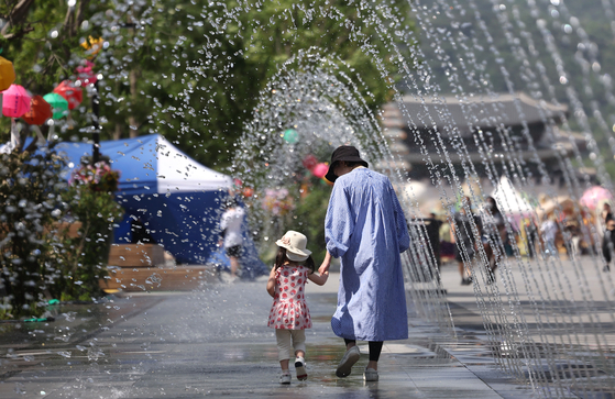 Passersby walk through a water fountain at Gwanghwamun Square in central Seoul on Wednesday as heatwaves descend on the country. [YONHAP]