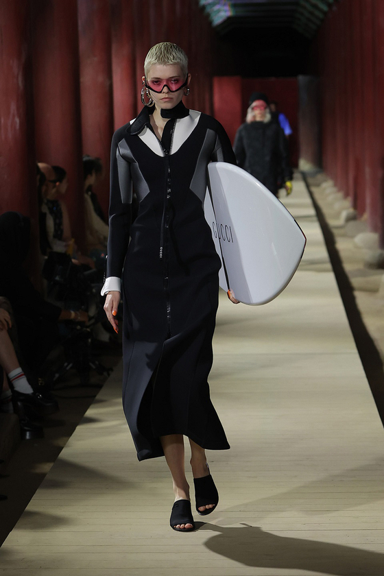 A model walks down Geunjeongjeon's haenggak, a roofed corridor, carrying a surf board for the latest Gucci 2024 Cruise collection show on May 16. [GUCCI] 