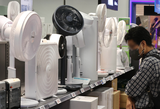A person stands in front of a fan stand at a discount store in Seoul on Sunday. [YONHAP]