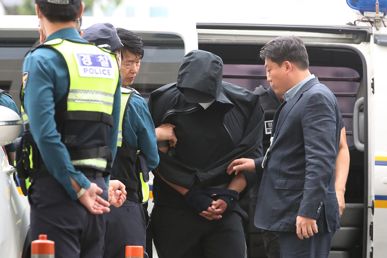 Police officials escort a man who opened an emergency exit door mid-flight on an Asiana Airlines plane to his warrant hearing at the Daegu District Court on Sunday. [NEWS1]