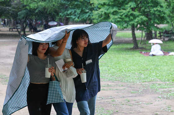 Visitors to Seoul Forest use a picnic mat to escape a shower on Tuesday afternoon. [YONHAP]