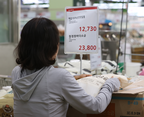 A person picks up a bag of salt at a discount store in Seocho District, southern Seoul, on Tuesday. Salt prices have surged due to reduced production from frequent rain and woes over the release of treated radioactive water from the Fukushima nuclear power plant. [YONHAP] 