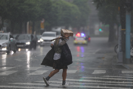 A man tries to cover his face from the rain in downtown Seoul Wednesday. The shower earlier in the day took many Seoulites by surprise. According to the Korea Meteorological Administration, scattered showers are expected to fall in Seoul and eastern Gyeonggi on Thursday as well as in Gangwon and North Chungcheong. [YONHAP]