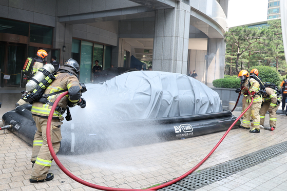Firefighters blast water on an electric vehicle placed in an EV tank during a private-public fire drill held at Tower Palace in Gangnam, southern Seoul, Wednesday. While EV sales have been growing rapidly, an increasing number of EVs are catching fire, including a Tesla that caught fire on the road in Jeonju, North Jeolla, on June 5. It took three hours for the fire department to put it out. [YONHAP]