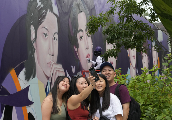 Tourists take a selfie in front of a mural of K-pop band BTS members to celebrate its 10th debut anniversary on the outer wall of a building in central Seoul on Wednesday. [AP/YONHAP]