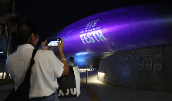 A tourist on June 12 takes a photo of the Dongdaemun Design Plaza (DDP) building in central Seoul, covered in a purple façade to celebrate the 10th anniversary of BTS's debut. [YONHAP]