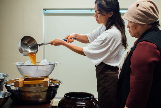 Ae Jin Huys, left, learns the process of filtering the liquid after the fermentation process of meju (dried fermented soybeans) with water and salt from Koh Eun-jeong, Huys' first "teacher," and mentor to many other Korean homemakers and renowned chefs. [YOLANTA C. SIU] 