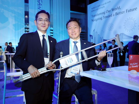 SK Inc Chairman Chey Tae-won, right, holds up his crutches with the Busan World Expo logo alongside Samsung Electronics Executive Chairman Lee Jae-yong during Korea's World Expo reception event in Paris Wednesday. [YONHAP]