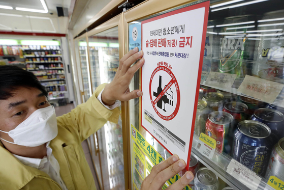 An official puts a sticker on a refrigerator door saying that alcohol and tobacco sales to people under the age of 19 are prohibited at a convenience store in Buk District, northern Gwangju, on Tuesday. Korea adopted the international method of counting age starting Wednesday, however, the legal age to drink and smoke are unaffected by the change. [BUK DISTRICT]