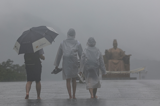Passersby walk across Gwanghwamun Square in central Seoul barefeet on Tuesday afternoon amid the rain. [YONHAP]