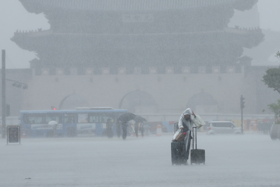 A tourist wrestles with carrying her luggage amid the rain at Gwanghwamun Square. [YONHAP]