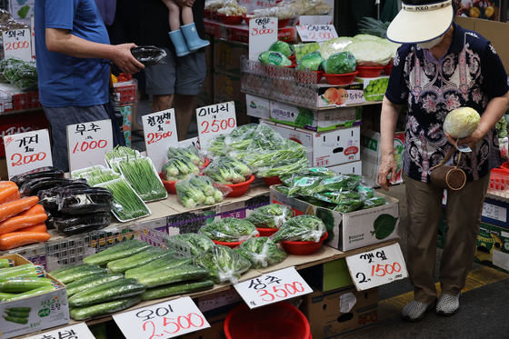 A customer shops for groceries at a vegetable stall at Mangwon Market in Mapo District, western Seoul, on Sunday. Grocery prices are on the rise following recent heavy rainfalls and heatwaves, with the price of spinach soaring nearly 130 percent in July compared to the previous month and lettuce 72 percent. Cucumber prices rose 67 percent from the previous week. [YONHAP]