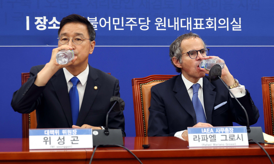 Rafael Grossi, director general of the International Atomic Energy Agency, right, drinks water out of a bottle next to the Democratic Party Rep. Wi Seong-gon at the National Assembly on Sunday. The meeting was evaluated to have failed in meeting eye-to-eye on the safety of the Fukushima Daiichi Nuclear Power Plant’s treated radioactive water. [YONHAP]