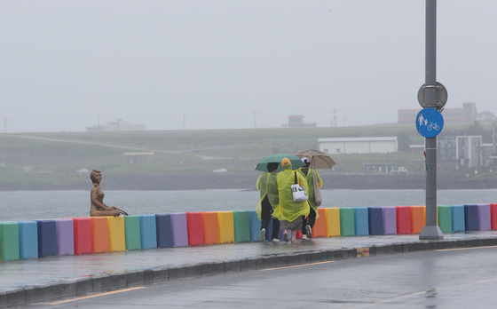 Tourists in raincoats and holding up umbrella walks along Jeju city on Sunday. [YONHAP]