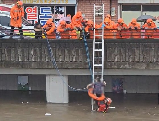 Firefighters rescue a person from a stream in Sasang District, Busan, on Tuesday as heavy rain battered the area and raised the stream's water level. [BUSAN METROPOLITAN CITY FIRE DEPARTMENT]