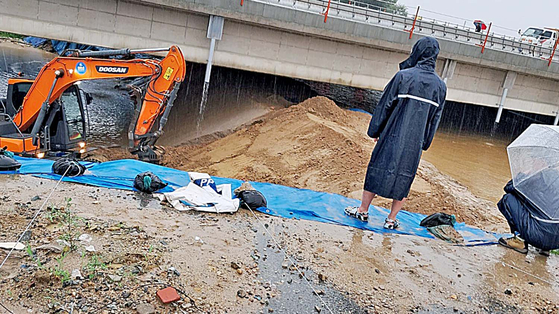 An excavator stacks up sand on a temporary levee next to the Miho River on Friday. The levee on Saturday morning broke, flooding a nearby underpass where nine people were found dead as of Sunday. [JOONGANG ILOB] 