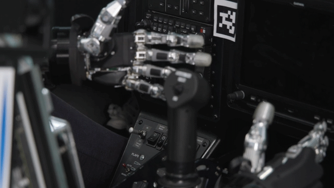 Pibot, a humanoid pilot robot developed by a KAIST research team, grabs a flight control stick in the cockpit of a flight simulator. [KAIST]