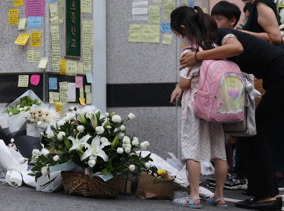 A student, with her mother, pays condolences to a teacher who took her own life in a classroom earlier this week at Seoul Seo 2 Elementary School in Seocho District, southern Seoul on Thursday. Hundreds of flower wreaths and baskets were delivered to the school gates for a makeshift altar for the late 23-year-old teacher, and many people left notes conveying their condolences to her on the walls. [YONHAP]