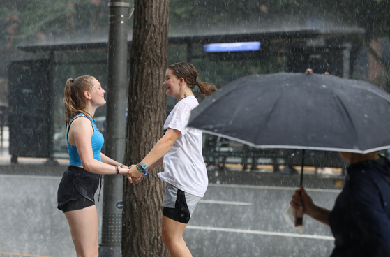 Two girls dance during a downpour in Myeong-dong of Jung District, central Seoul, on Monday. The unexpected, heavy downpour only lasted for a short period in just a few areas of the nation’s capital. Other parts of the city only experienced heavy heat. [NEWS1]