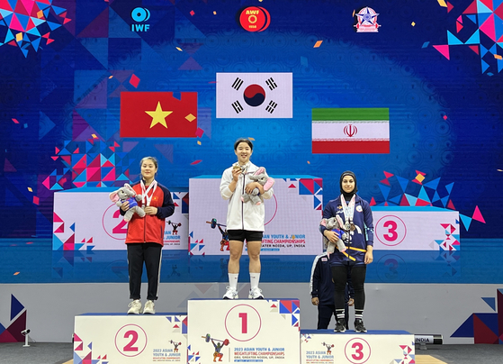 Korea's Han Ji-hye, center, poses on the podium after taking the gold medal in the women's 59 kilograms at the 2023 Asian Youth & Junior Weightlifting Championships on Tuesday in Delhi. Han topped the podium after lifting 84 kilograms in the snatch discipline and 109 kilograms in the clean and jerk. [YONHAP]