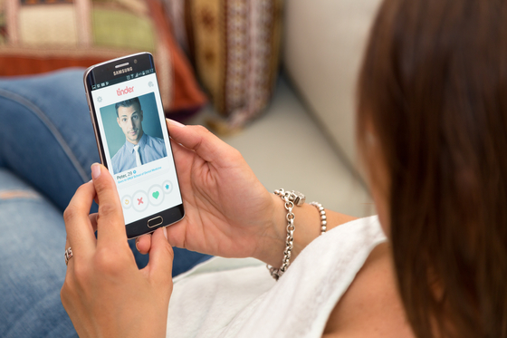 A woman holds a smartphone with Tinder open on the screen. [SHUTTERSTOCK]