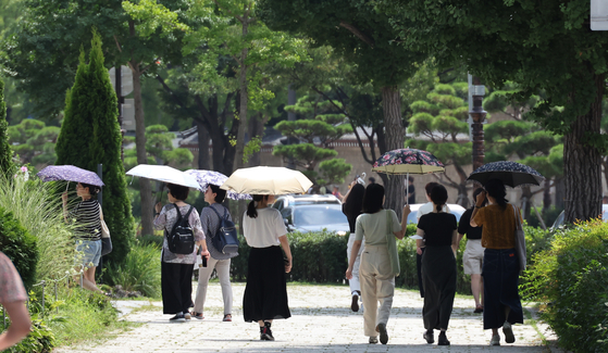 Pedestrians carry umbrellas to avoid sunlight in a street in Samcheong-dong, central Seoul, on Thursday. [YONHAP]