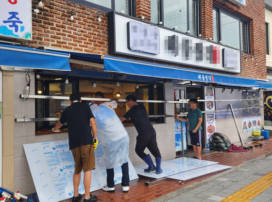 People install flood barriers to prepare for the approaching Typhoon Khanun at a restaurant near Songdo Beach in Busan on Wednesday. More than 400 millimeters (15.7 inches) of rain is expected to fall in the inland areas of western South Gyeongsang and North Gyeongsang, and along the Gyeongsang coastal regions until Thursday, according to the Korea Meteorological Administration. [YONHAP]