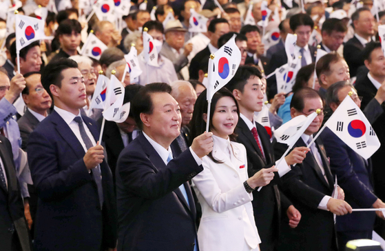 President Yoon Suk-yeol, center left, and first lady Kim Keon-hee wave the Korean national flag at a ceremony celebrating the 78th Liberation Day in an auditorium at Ewha Womans University in Seodaemun District, central Seoul Tuesday. [JOINT PRESS CORPS] 