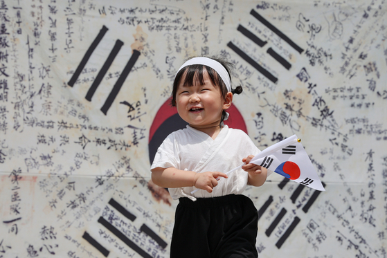 A child holds a Korean national flag as she stands in front of a display of a flag signed by the Korean Liberation Army which fought against Japan to free Korea from colonial rule in Jongno District, central Seoul, as people nationwide celebrated the 78th Liberation Day anniversary Tuesday. [YONHAP] 