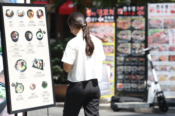 A pedestrian walks past food menu boards in a street in Seoul on Monday. [YONHAP]