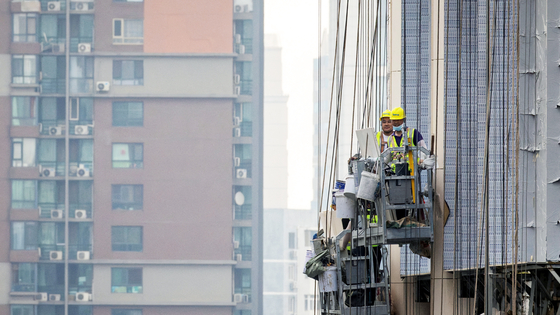 Construction workers hang outside an apartment building in Beijing on July 29. [REUTERS]