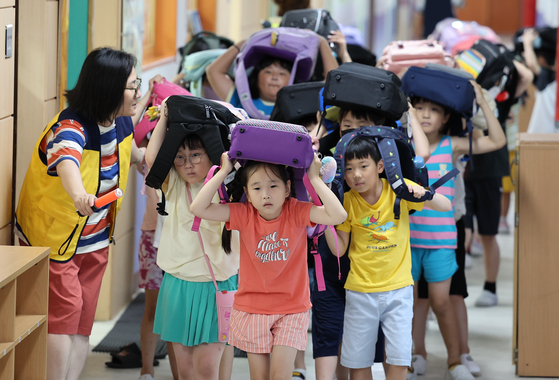 Students at Jeongja Elementary School in Sunwon evacuates from class while covering their heads with backpacks as the siren from the civil defense drill set off at 2 p.m. on Wednesday. The country came to a standstill including 216 roads that were locked down when the first full-scale civil defense drill in six years was set off for 20 minutes. [YONHAP]