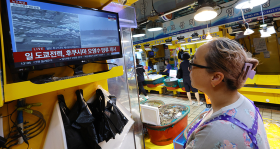 A fish shop owner at the fish market in Incheon watches the breaking news of Tokyo Electric Power Company releasing the treated radioactive water from the Fukushima Daiichi nuclear power plant into the ocean on Thursday. [YONHAP]