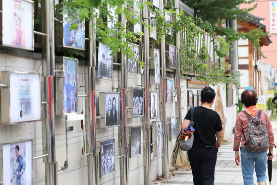 Pedestrians pass by a photo wall commemorating Jeong Yul-sung along a road named after him at Nam District in Gwanju on Monday. [YONHAP]