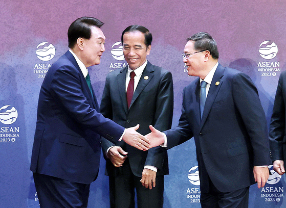 Korean President Yoon Suk Yeol, left, shakes hands with Chinese Premier Li Qiang, right, with Indonesian President Joko Widodo, center, looking on at the Asean Three Summit held at the Balai Sidang Jakarta Convention Center in Indonesia Wednesday. [JOINT PRESS CORPS] 