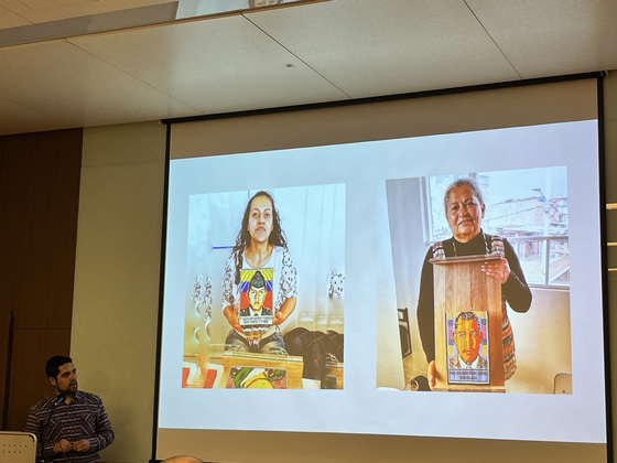 Mateo Perea Bernal, artist and founder of Tejidos Chakana, left, shows photos of women in Colombia who participated in the organization's workshops to produce beadwork portraits of the sons they lost during Colombia's civil conflicts. [ESTHER CHUNG]