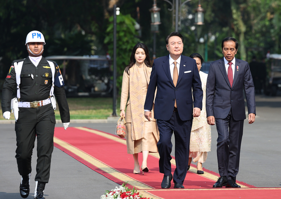 President Yoon Suk Yeol, left in the front row, and Indonesian President Joko Widodo, right, walk side by side at the Jakarta Presidential Palace on Friday during Yoon's visit to the Southeast Asian country, while first ladies Kim Keon Hee and Iriana Joko Widodo trail behind. [JOINT PRESS CORP]
