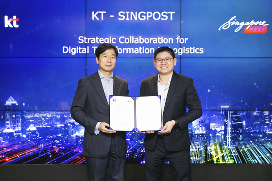 Choi Kang-rim, head of KT’s AI mobility business, and Eric Yeo, head of SingPost’s business technology solutions and property, pose for a photo after signing a memorandum of understanding at KT’s office in Songpa District, southern Seoul, on Thursday. [KT]